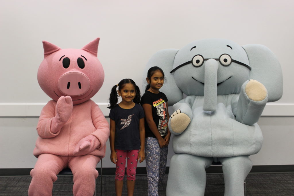 Elephant and Piggie characters sitting with kids at the library