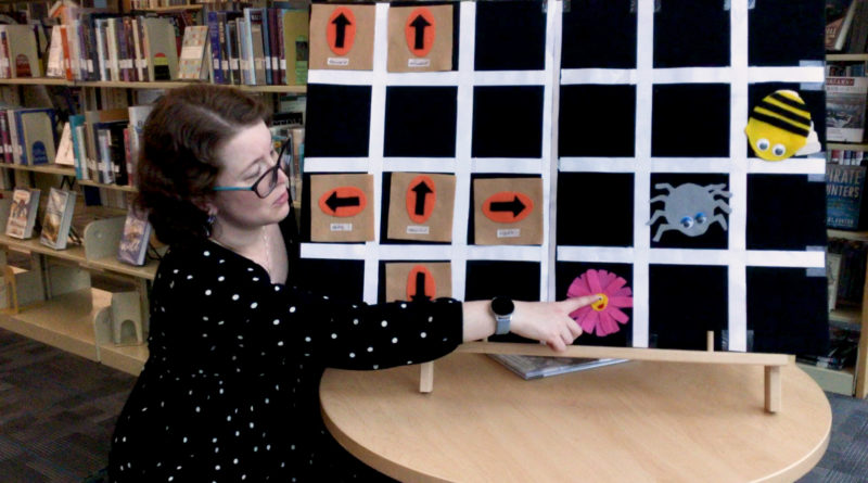 Library staff using a flannel board with a grid, pointing to a fabric flower