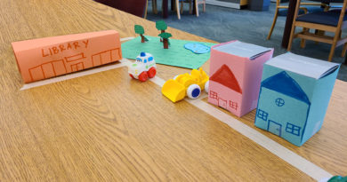 A city made up on paper on a table with a tape street and plastic toys