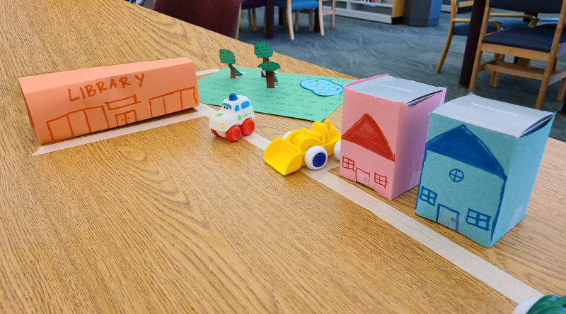 A city made up on paper on a table with a tape street and plastic toys