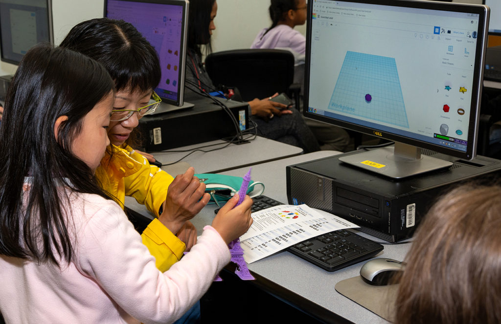 A parent and child looking at a 3D object while sitting at a computer