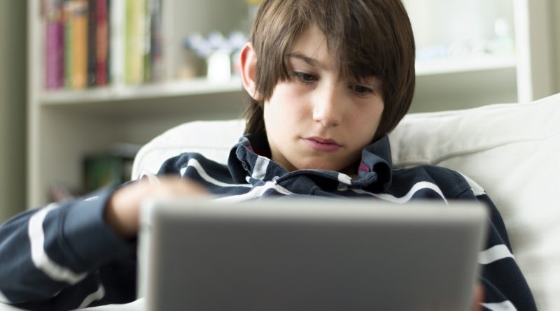Young boy holding tablet while sitting on a chair